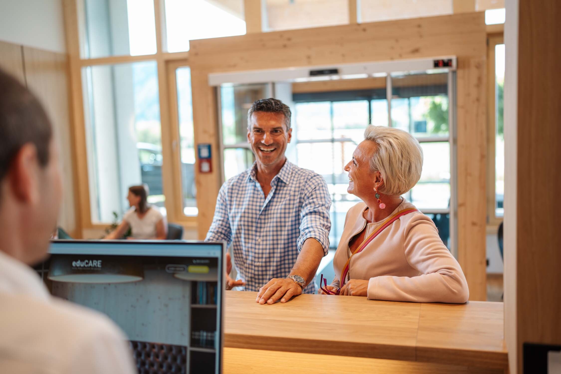 Ein Mann und eine Frau lächeln an einem Empfangstresen im eduCARE Hotel.