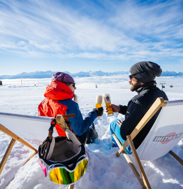 Eine Frau und ein Mann liegen in einem Liegestuhl und stoßen mit zwei Biergläsern an.