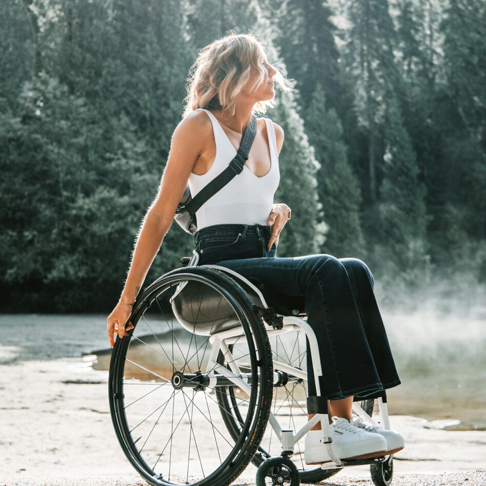 Eine Frau im Rollstuhl genießt die Aussicht in einem Waldgebiet.