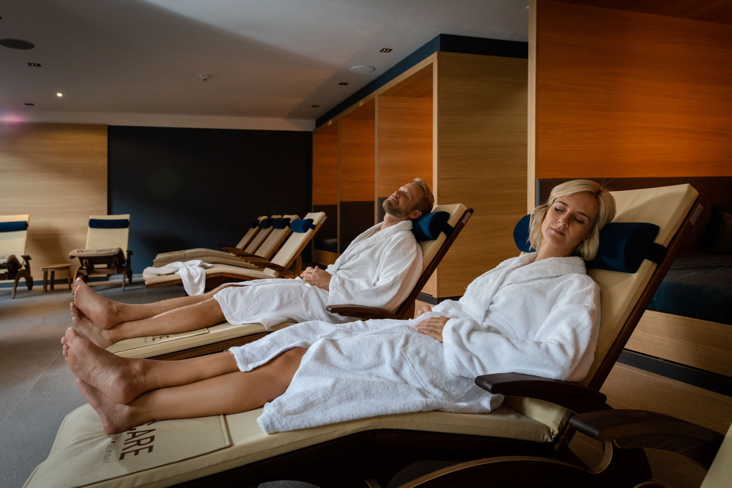 Couple relaxing in lounge chairs wearing white robes in the spa area of hotel educare.