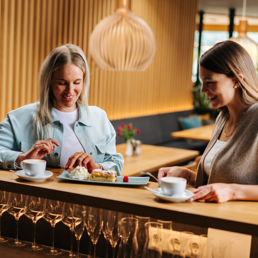 Zwei Frauen genießen Kaffee und Kuchen im Wirtshaus "Zum Treffner" mit moderner Holzeinrichtung.