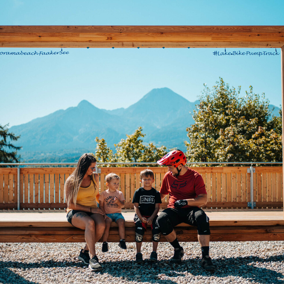 Eine Familie sitzt auf einer Bank im Pumptrack Drobollach mit Blick auf die Berge.