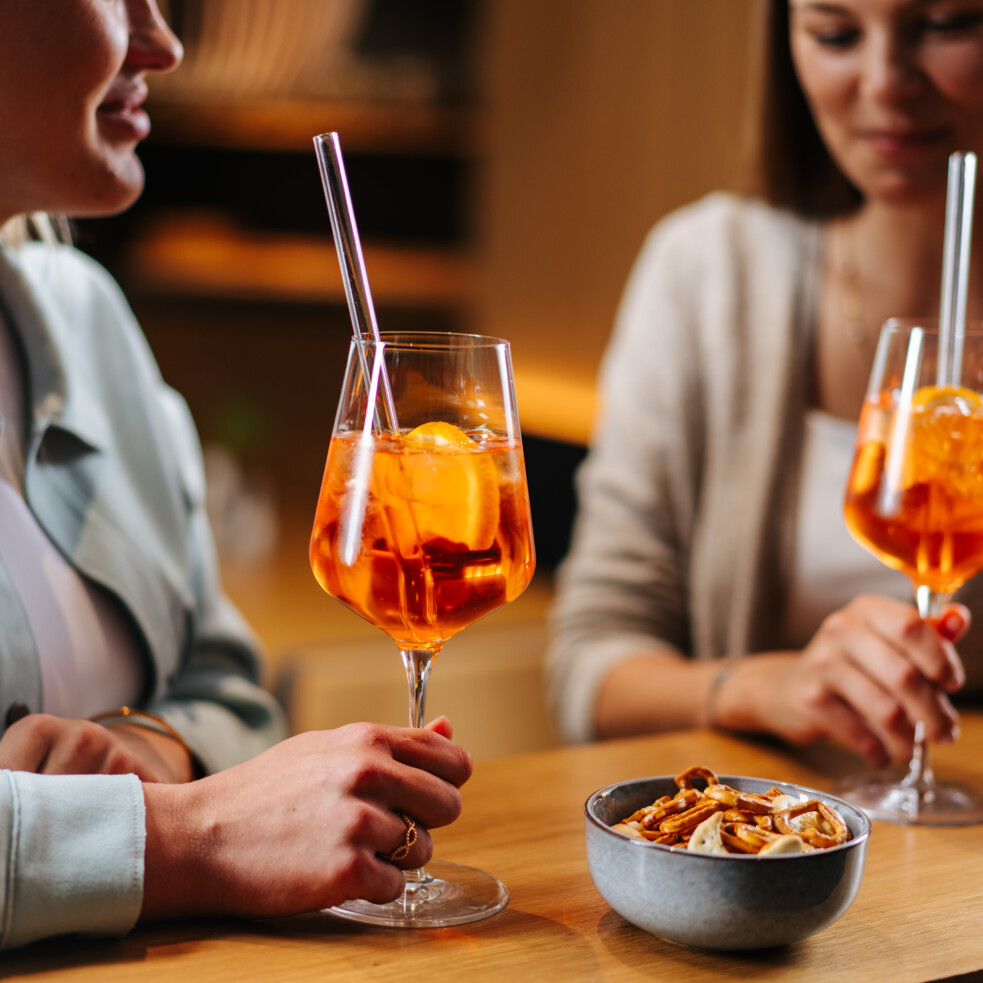 Zwei Personen genießen Drinks an einer Bar, daneben eine Schale mit Snacks.