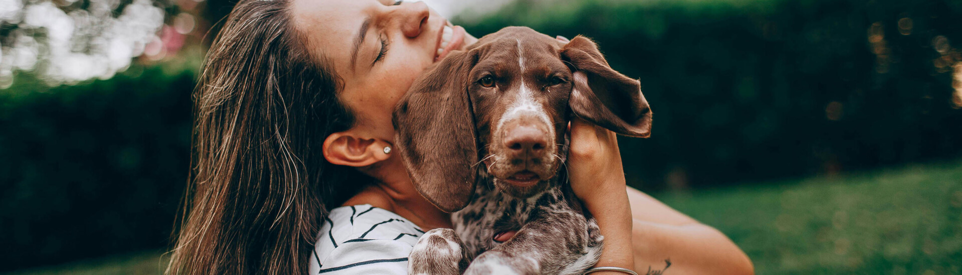 Eine Frau umarmt glücklich einen braunen Hund im Garten.