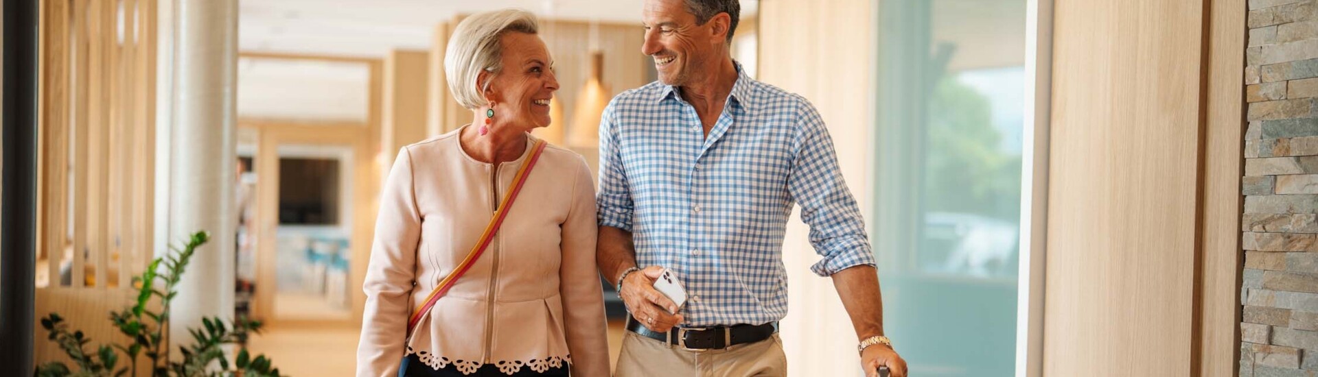 Ein Paar geht lächelnd mit einem Koffer durch einen hellen Flur.