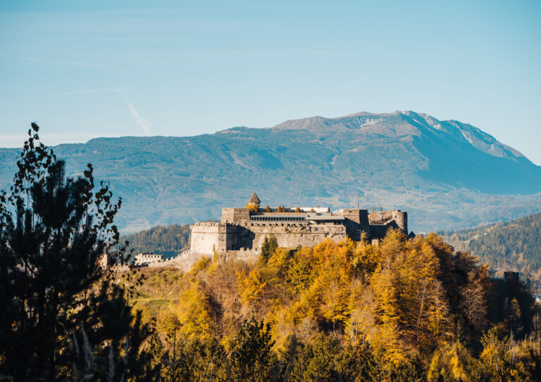 Burg Landskron im Herbst, umgeben von herbstlichen Bäumen und einer Berglandschaft.