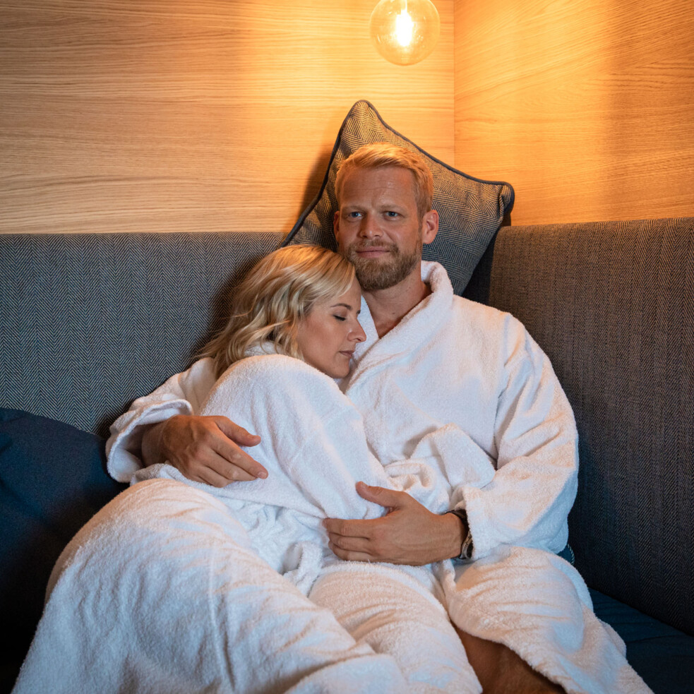 A couple in white bathrobes cuddling on a cozy sofa in the spa area of Hotel Educare. 