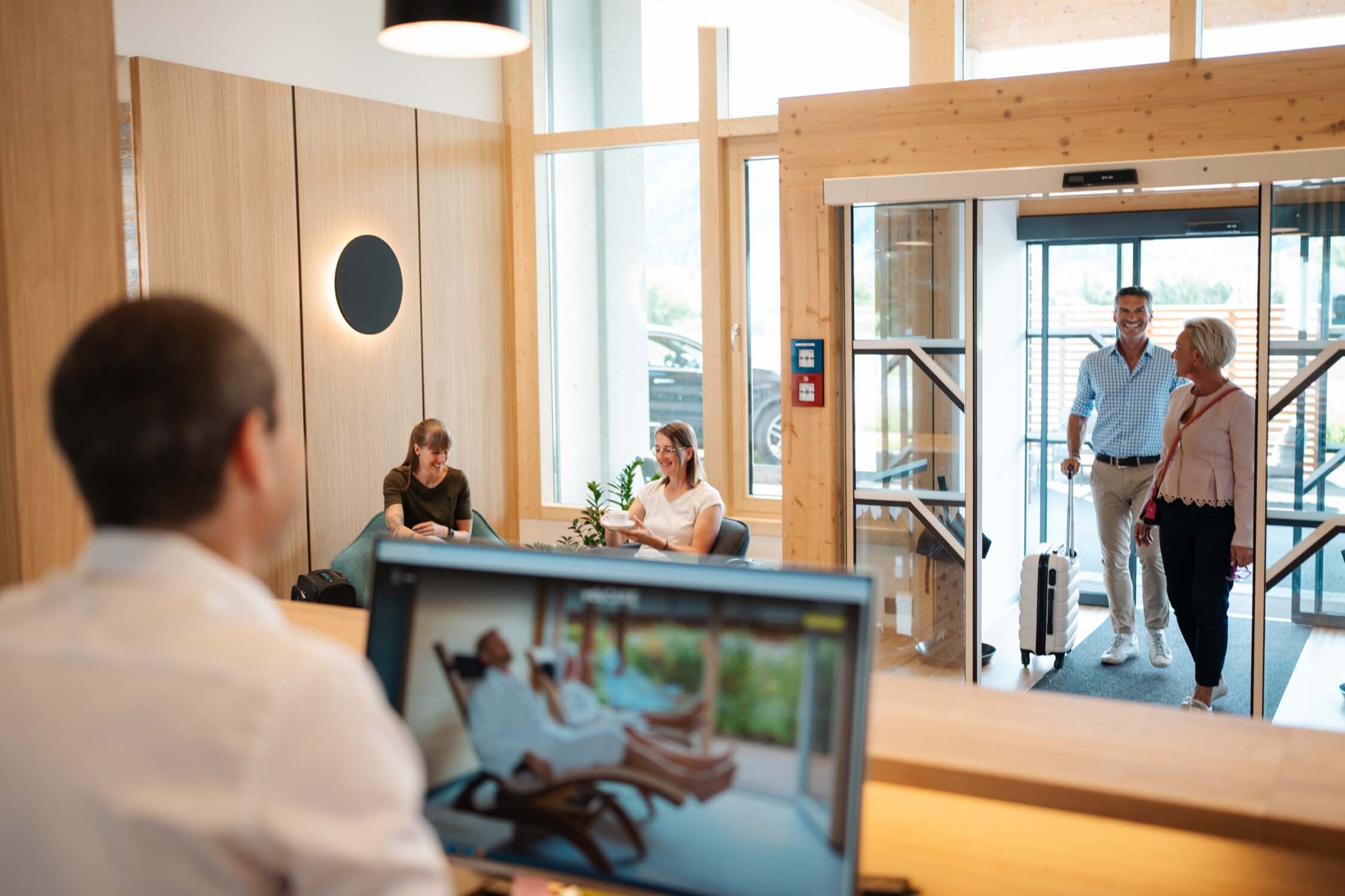 Die Gäste betreten die Hotellobby mit hellem Holzdekor, während ein Rezeptionist am Schalter arbeitet.