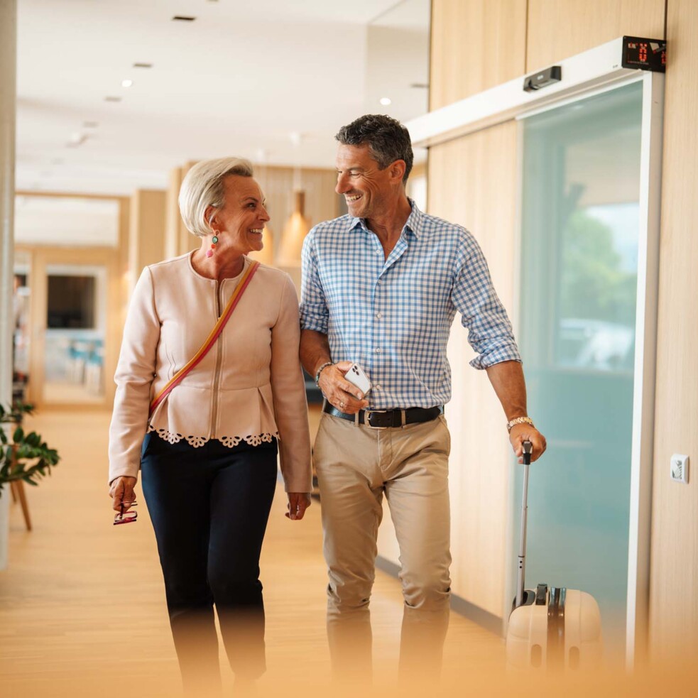 A smiling couple walks through a hallway of the Hotel Educare with a suitcase.