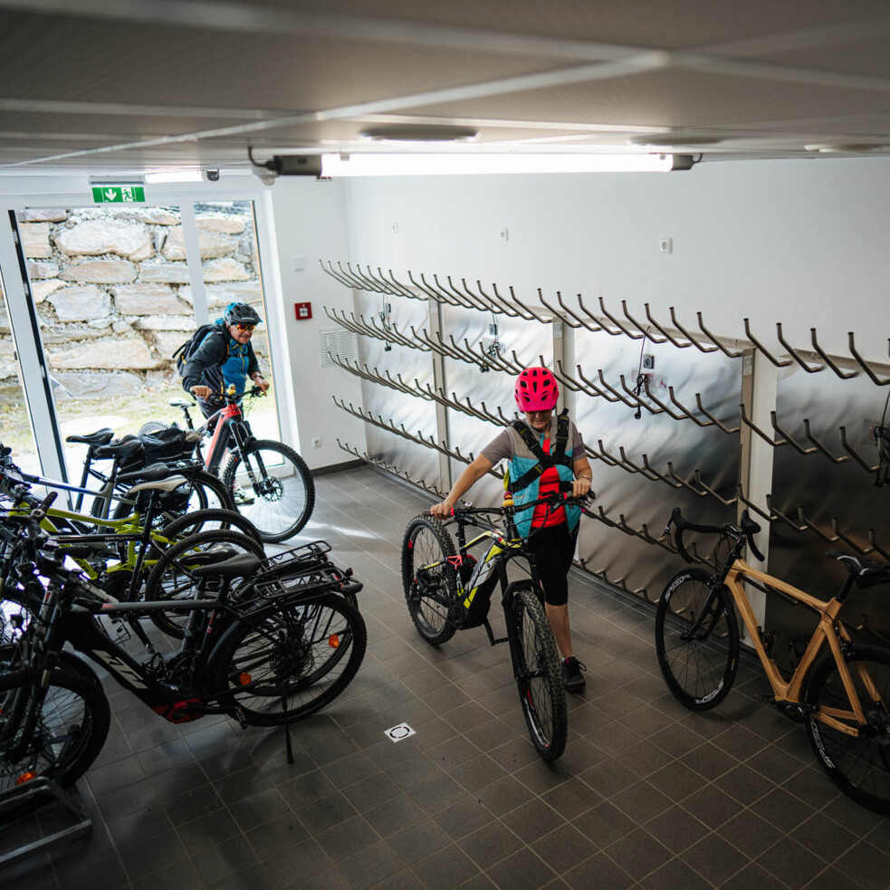 Personen parken Fahrräder in einem modernen Fahrradraum mit Wandhalterungen.