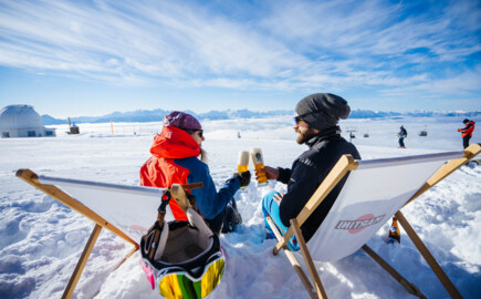 Eine Frau und ein Mann liegen in einem Liegestuhl und stoßen mit zwei Biergläsern an.