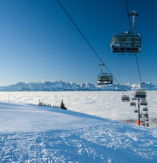 Sessellift über schneebedecktem Berg mit Blick auf Wolkenmeer und Alpenpanorama.