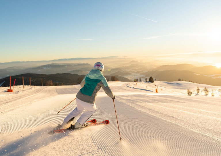 Frau fährt Ski auf einer frisch präparierten Piste bei Sonnenaufgang