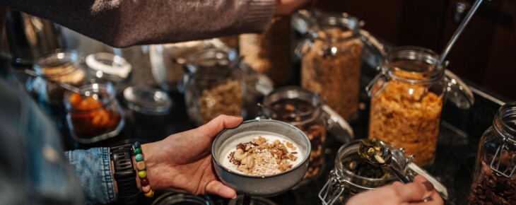 Eine Person füllt eine Schüssel mit Müsli aus mehreren Gläsern an einem Buffet.