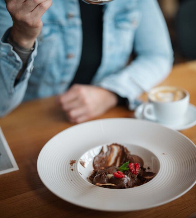 Eine Person isst ein Schokoladendessert mit Himbeeren und Minze und trinkt einen Kaffee.