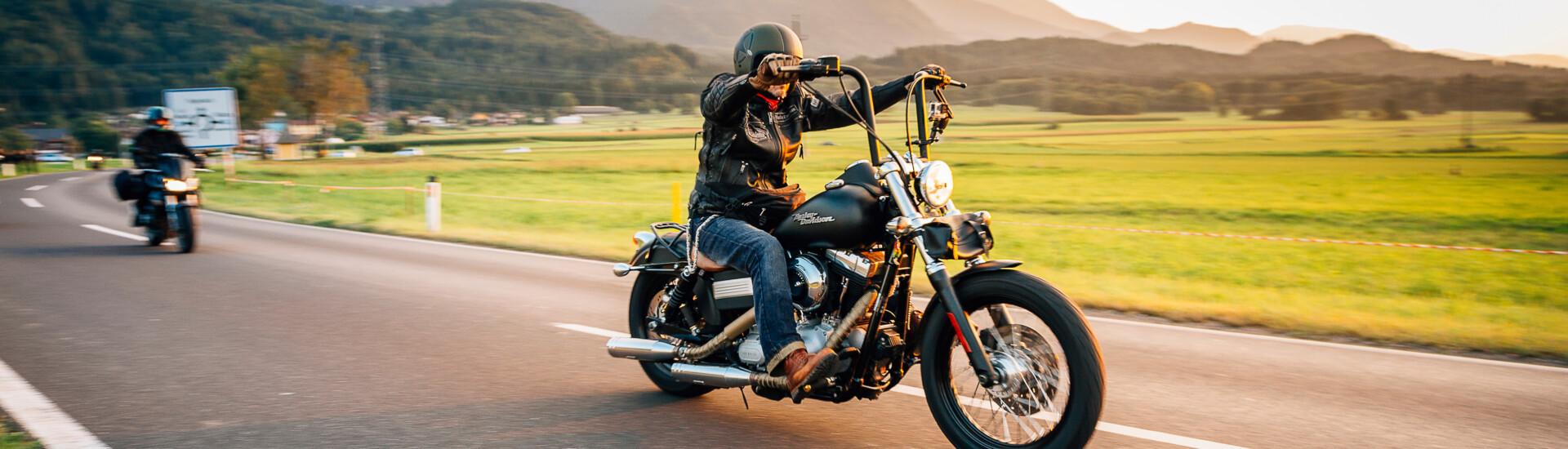 Motorradfahrer auf malerischer Landstraße mit Bergblick, bei Sonnenuntergang.