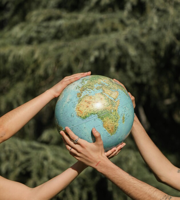 Mehrere Hände halten gemeinsam einen Globus, im Hintergrund befinden sich Bäume.