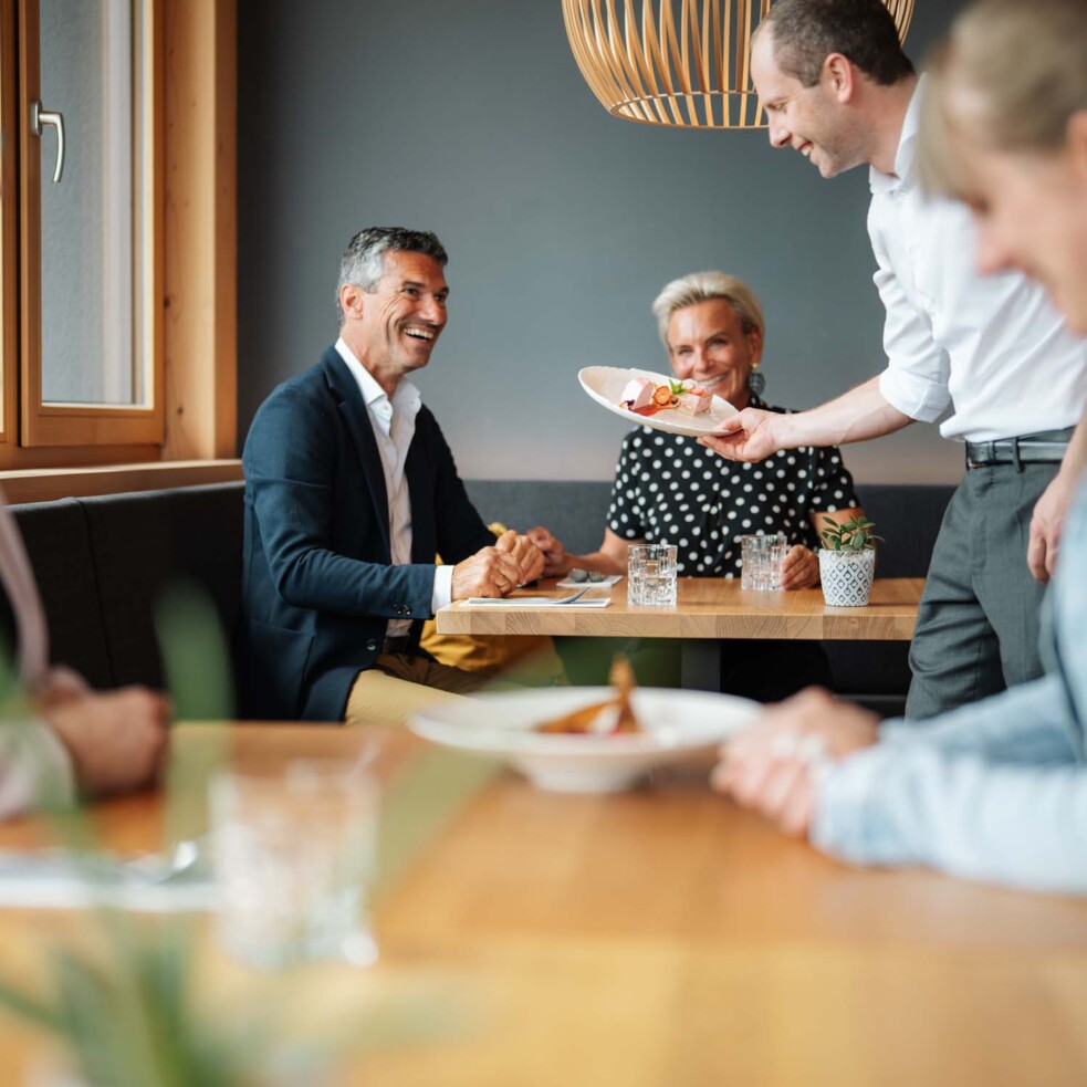 Personen sitzen im Restaurant, ein Kellner serviert die bestellten Gerichte.