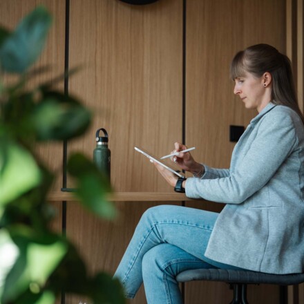 Eine Frau sitzt in einem modernen Zimmer und arbeitet an einem Tablet. 