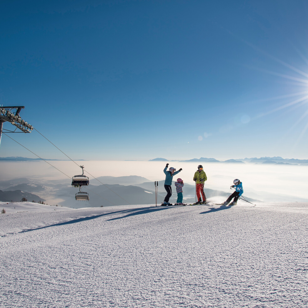 Skiers enjoy a sunny day on the Gerlitzen Alpe, near a ski lift, with distant mountains in the background.
