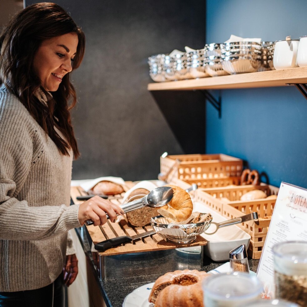 Eine Frau bedient sich am Frühstücksbuffet mit Gebäck und Müsli.