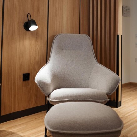 Ein grauer Sessel mit Hocker vor einer Wand mit Holzverkleidung in einem modernen Raum.