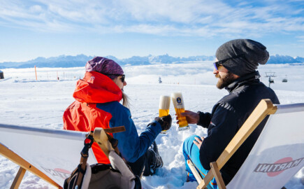 Eine Frau und ein Mann liegen in einem Liegestuhl und stoßen mit zwei Biergläsern an.