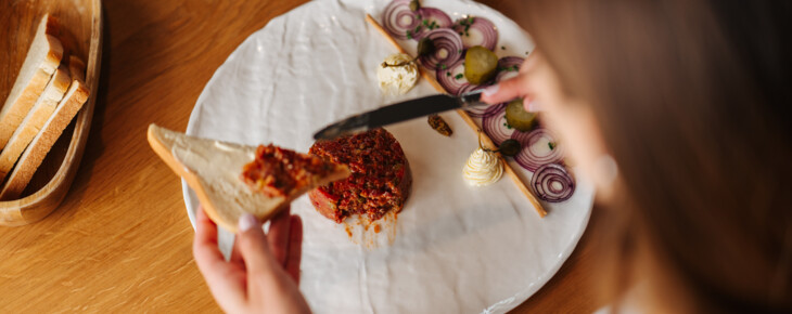 Eine Person streicht Beef Tartar eine halbe Scheibe Toastbrot.