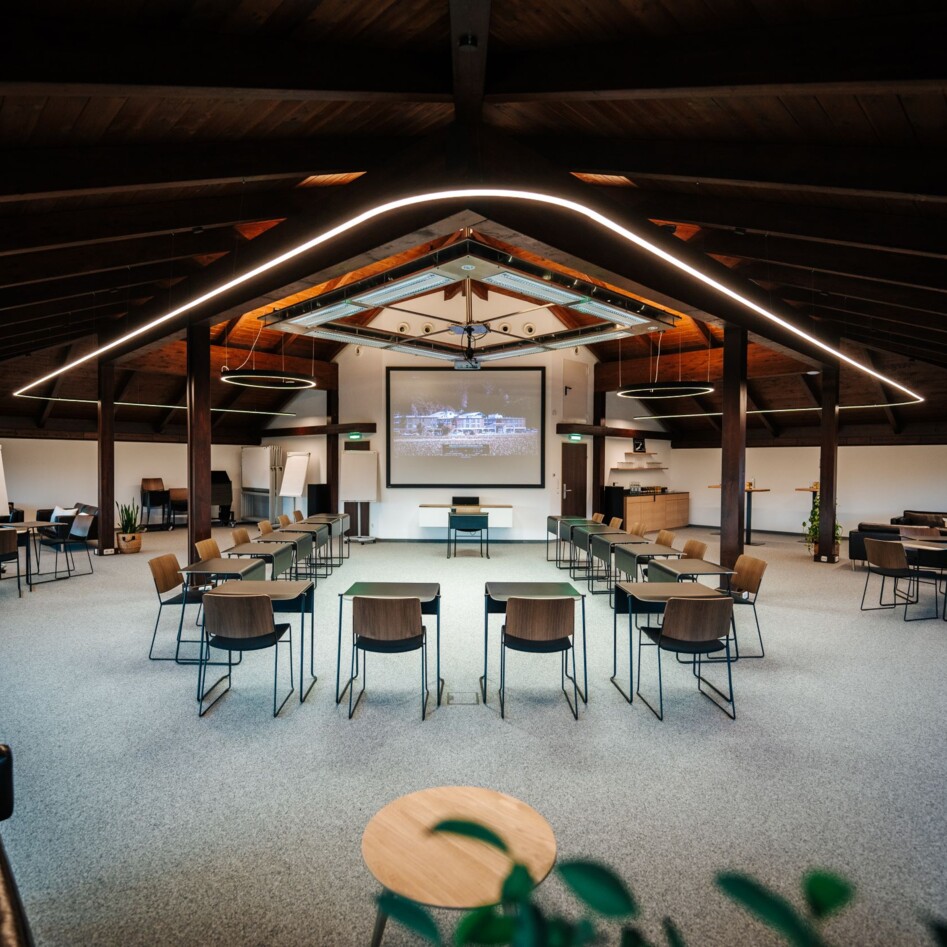 Spacious conference room with modern design, featuring rows of chairs, a large screen for presentations, and ambient lighting.