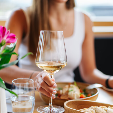 Eine Dame sitzt am Tisch mit einem Essen und einem Glas Wein.