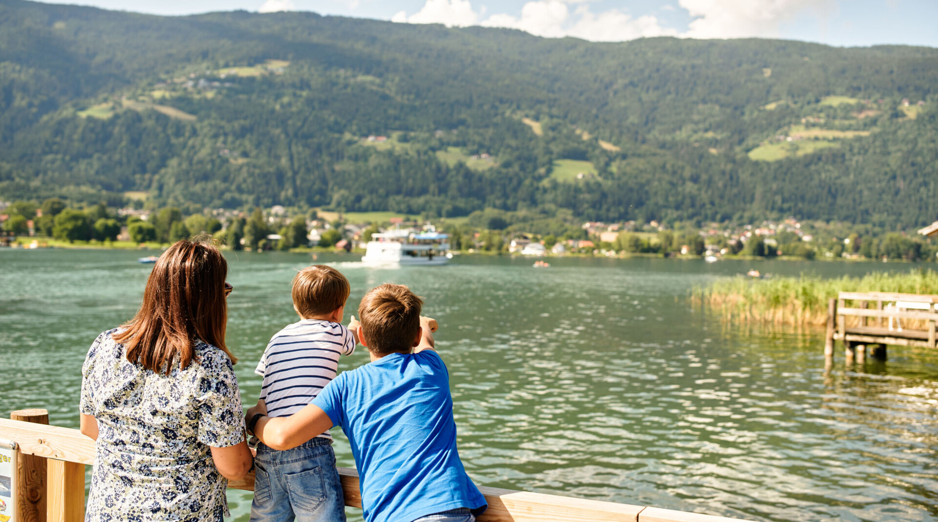 A woman and two children watch a boat on Lake Ossiach.