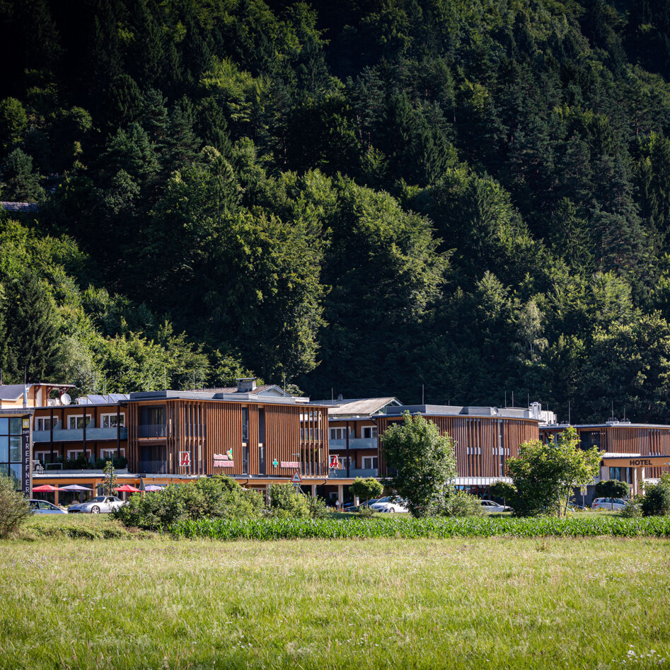 Das Hotelgebäude des Hotel eduCARE vor einem bewaldeten Hügel, umgeben von Grünflächen.